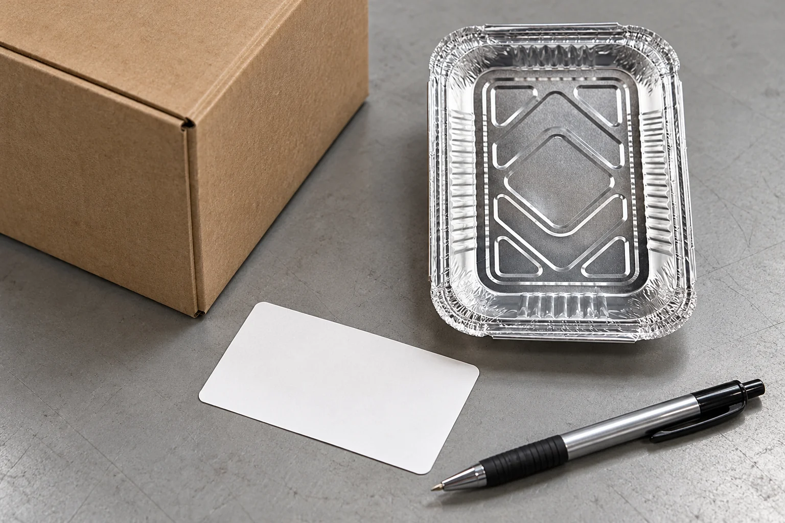Plain carton corner, blank unattached label, separate pen and empty foil tray on a grey bench