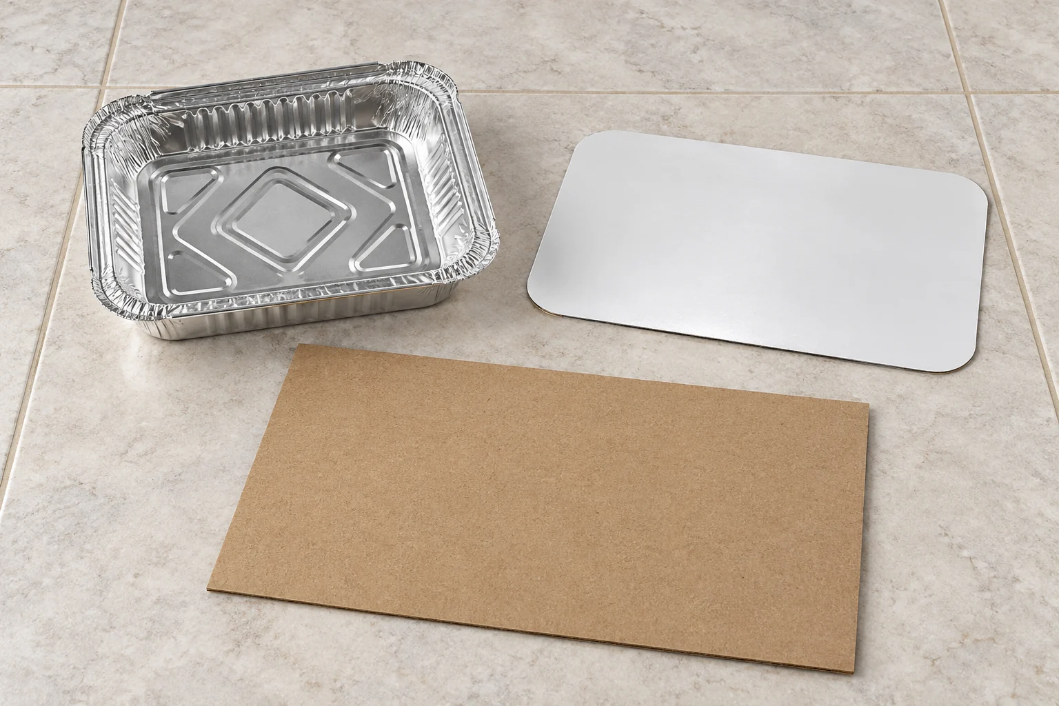 Empty foil tray, detached white-faced lid and flat carton panel separated on a tiled bench
